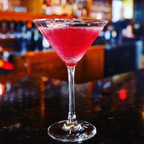 A vibrant pink cocktail served in a classic martini glass on a dark bar countertop.
