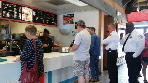 A line of customers waiting to order at a fast-food restaurant, with a cashier serving at the counter.