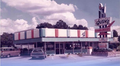 A vintage fast-food restaurant with a colorful exterior and a large sign reading "Rush's Hamburgers."