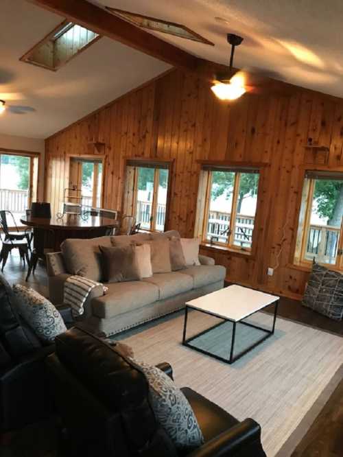 Cozy living room with wooden walls, large windows, a sofa, and a coffee table, overlooking a deck.