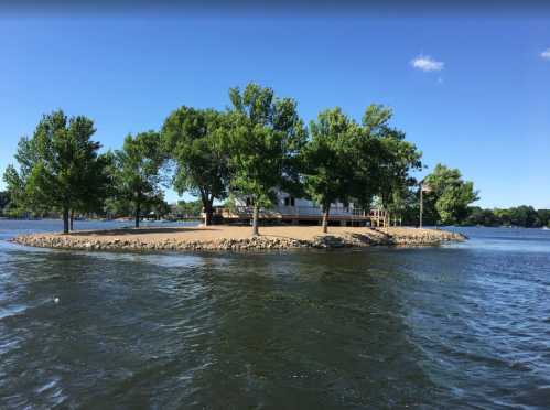 A small island with trees and a house, surrounded by water under a clear blue sky.