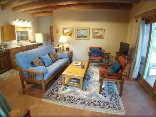 Cozy living room with a blue sofa, wooden furniture, a coffee table, and artwork on the walls, featuring warm lighting.