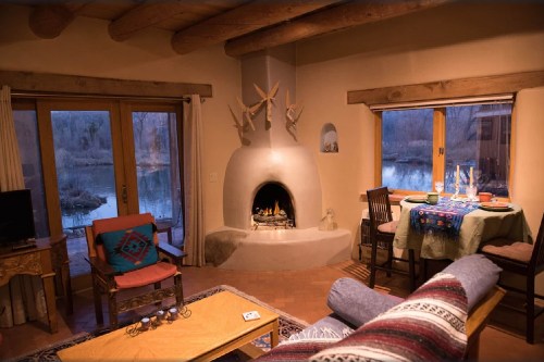 Cozy interior of a rustic cabin with a fireplace, dining area, and views of a serene outdoor landscape.