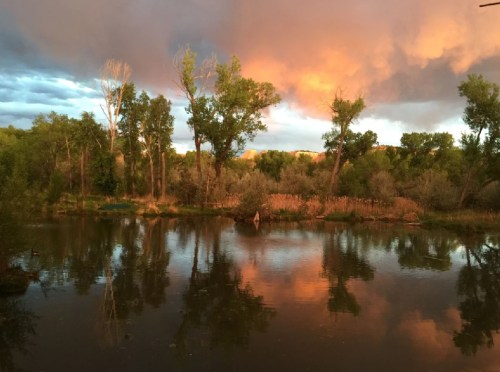 A serene river scene at sunset, with colorful clouds reflecting on the water and lush trees lining the shore.