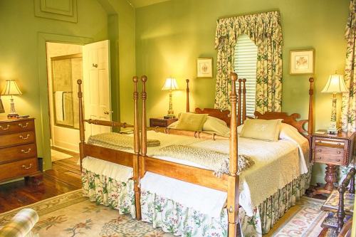 Cozy bedroom with a four-poster bed, green walls, floral curtains, and a bathroom doorway in the background.