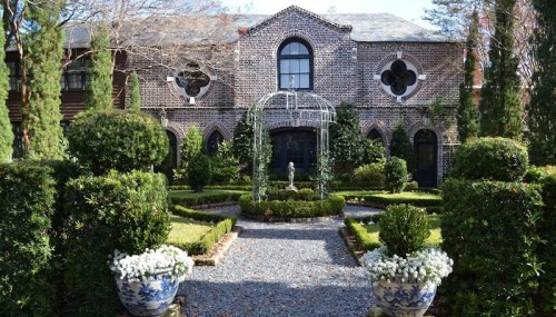 A beautifully landscaped garden with manicured hedges, a stone pathway, and a charming brick house in the background.