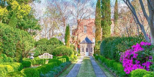 A picturesque garden path lined with vibrant flowers and neatly trimmed hedges, leading to a charming stone building.