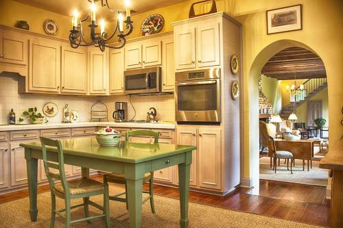A cozy kitchen with a green table, wooden cabinets, and a view into a warmly lit living area.