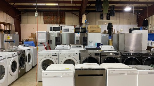 A warehouse filled with various appliances, including washers, dryers, and refrigerators, arranged in rows.