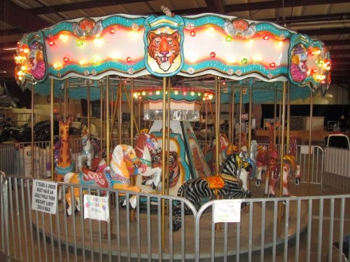A colorful carousel with illuminated lights and various animal figures, including horses and a tiger, in a fairground setting.
