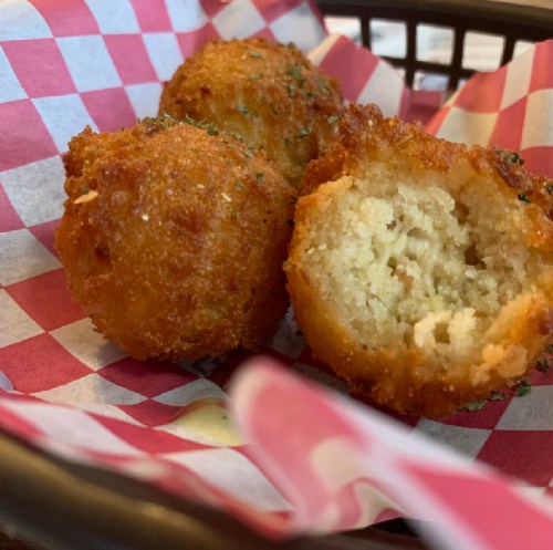 Three golden-brown fried balls, one cut in half, served in a basket lined with red and white checkered paper.