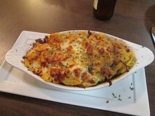 Baked pasta dish topped with melted cheese and herbs, served in a white dish on a plate.