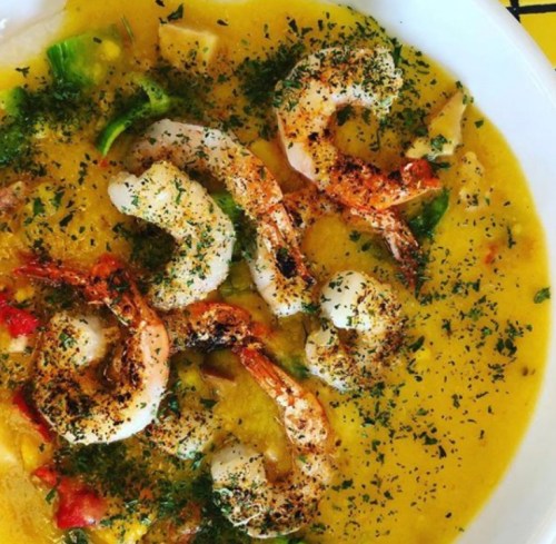 A vibrant dish featuring shrimp in a yellow sauce, garnished with herbs and vegetables.