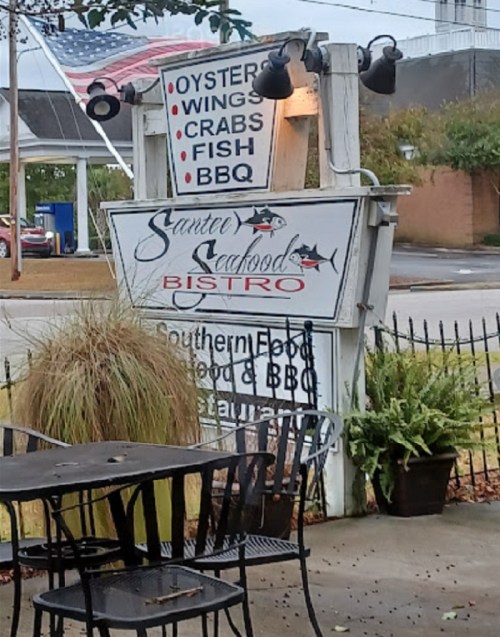 Sign for Sunter Seafood Bistro featuring oysters, wings, crabs, fish, and BBQ, with outdoor seating visible.