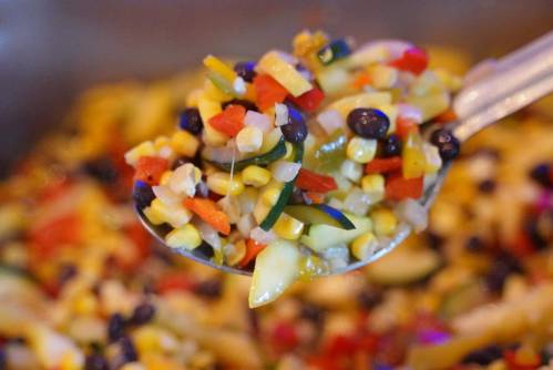 A close-up of a spoonful of colorful vegetable salad with corn, black beans, and diced peppers.