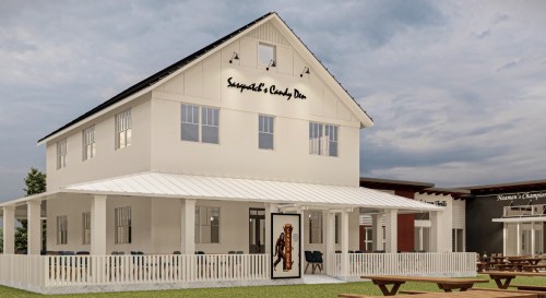 A white two-story building with a porch, featuring a sign that reads "Supper & Candy Den" and outdoor seating.