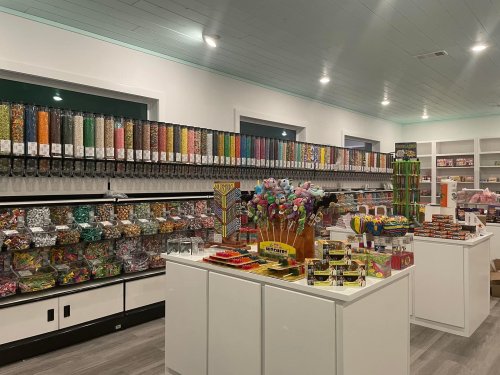 A colorful candy shop interior with shelves of jars filled with sweets and a display of various candies on white tables.