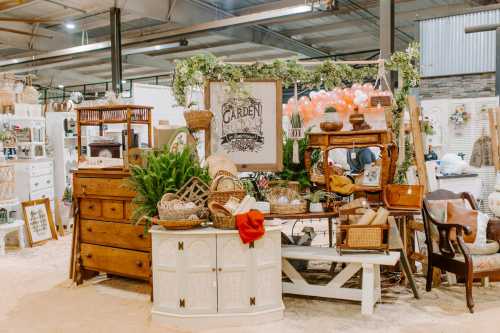 A cozy vintage market display featuring wooden furniture, baskets, and greenery, creating a charming garden atmosphere.