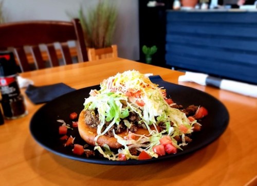 A colorful plate of food featuring a crispy base topped with seasoned meat, lettuce, tomatoes, and cheese.