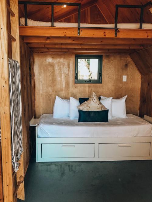 Cozy wooden interior of a small room featuring a bed with white pillows and a decorative black pillow.