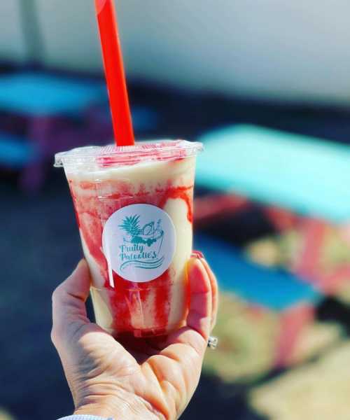 A hand holding a colorful drink with a red straw, featuring a label that says "Fruity Paradises."