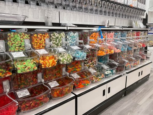 A colorful display of various candies in clear containers, arranged neatly on shelves in a candy store.