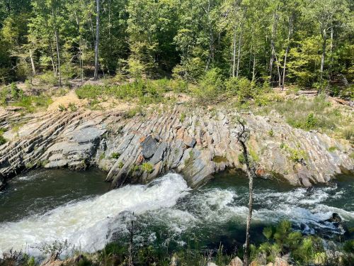 A flowing river cascades over rocky terrain, surrounded by lush green trees and vegetation.