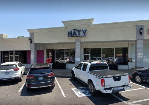 Exterior of a storefront labeled "NĀTV," with parked cars in front and a clear blue sky.