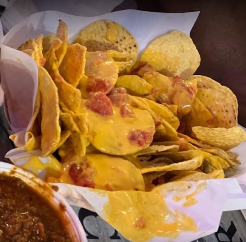A plate of nachos topped with melted cheese, diced tomatoes, and served with a side of chili.