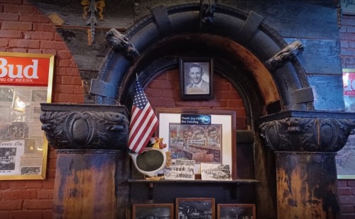 A rustic archway with a photo, American flag, and framed images on a brick wall in a cozy setting.