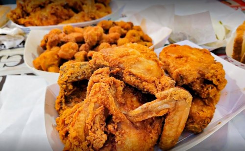 A close-up of crispy fried chicken pieces served with a side of fried snacks on a table.
