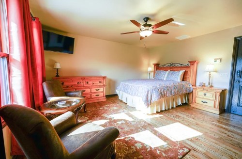 Cozy bedroom featuring a queen bed, wooden furniture, a TV, and warm lighting with a plush rug.