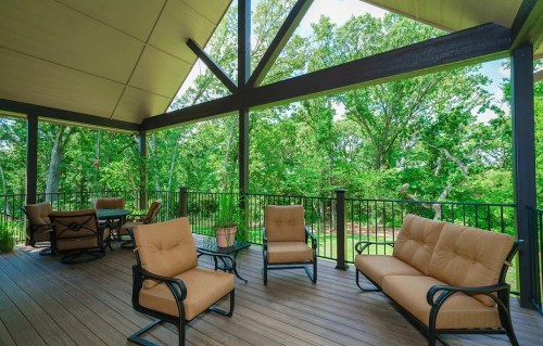 A spacious outdoor patio with comfortable seating, surrounded by lush greenery and trees under a shaded roof.