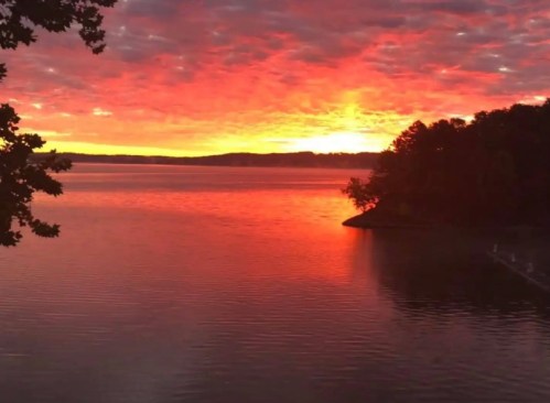 A vibrant sunset over a calm lake, with colorful clouds reflecting on the water's surface.