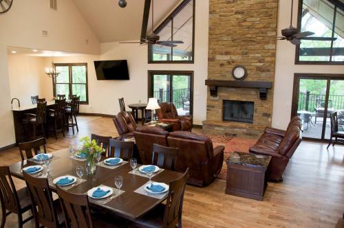 Cozy living and dining area with a stone fireplace, large windows, and wooden furniture in a modern cabin setting.