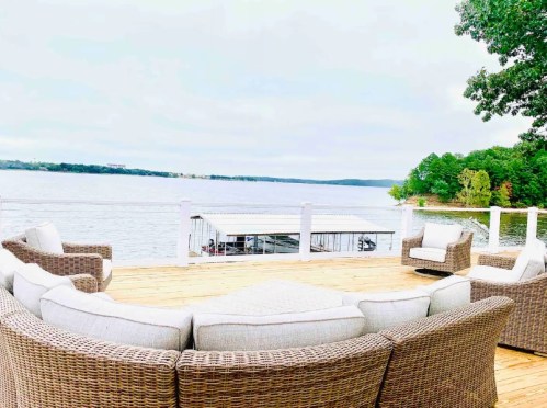 A cozy outdoor seating area with wicker chairs overlooking a calm lake and green trees in the background.