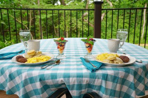 A table set for breakfast with two plates of eggs, sausage, biscuits, and fruit cups, surrounded by greenery.