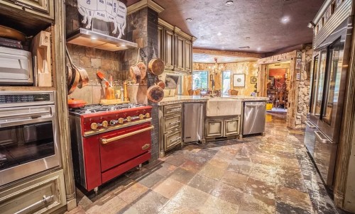 A spacious kitchen featuring a red stove, stone flooring, wooden cabinets, and modern appliances.