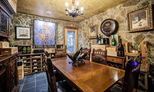 A rustic wine cellar featuring a wooden table, stone walls, and shelves filled with wine bottles and boxes.