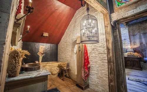 A rustic bathroom with a stone tub, wooden accents, and a vintage portrait on the wall, illuminated by a hanging light.