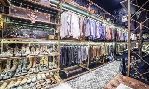 A stylish closet featuring neatly arranged shirts, shoes, and accessories on shelves with modern lighting.