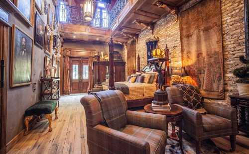 Cozy, vintage-style bedroom with wooden beams, stone walls, and elegant decor, featuring a bed and two armchairs.