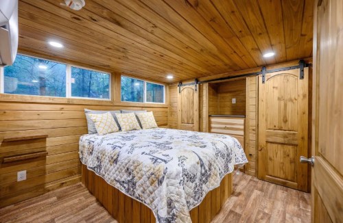 Cozy wooden bedroom with a queen bed, decorative quilt, and large windows for natural light.