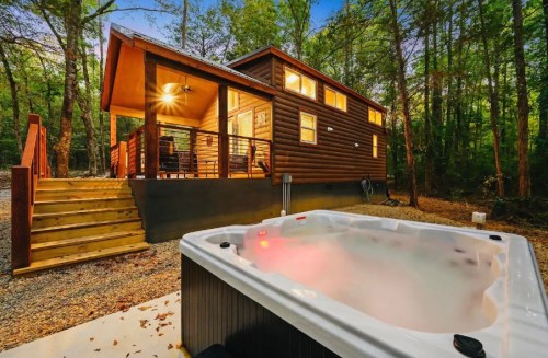 A cozy cabin in the woods with a hot tub in the foreground, surrounded by trees and a warm evening glow.