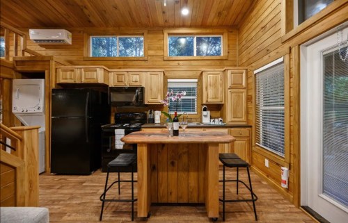 Cozy wooden kitchen with a central island, black appliances, and large windows letting in natural light.