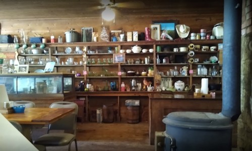 A rustic wooden shelf filled with various vintage items, jars, and kitchenware in a cozy, warm setting.