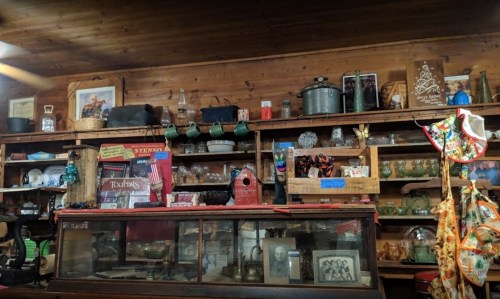 A rustic display of vintage items and antiques on wooden shelves, including glassware, jars, and decorative objects.