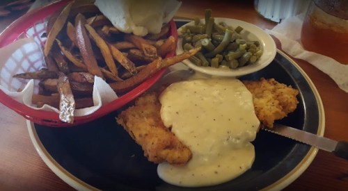 A plate of fried chicken with gravy, green beans, and a side of crispy fries in a basket.