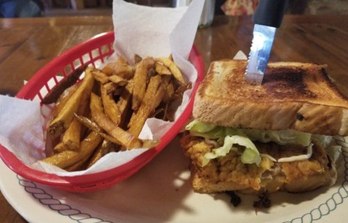 A toasted sandwich with lettuce and sauce, served with a side of crispy fries in a red basket.