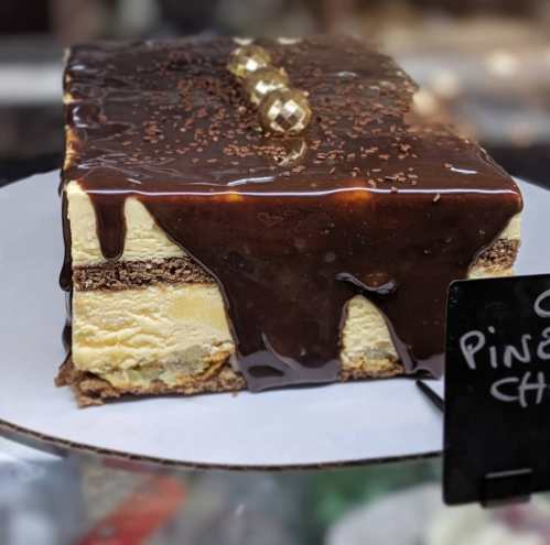 A rectangular cake with layers of ice cream, topped with chocolate sauce and decorative gold balls.